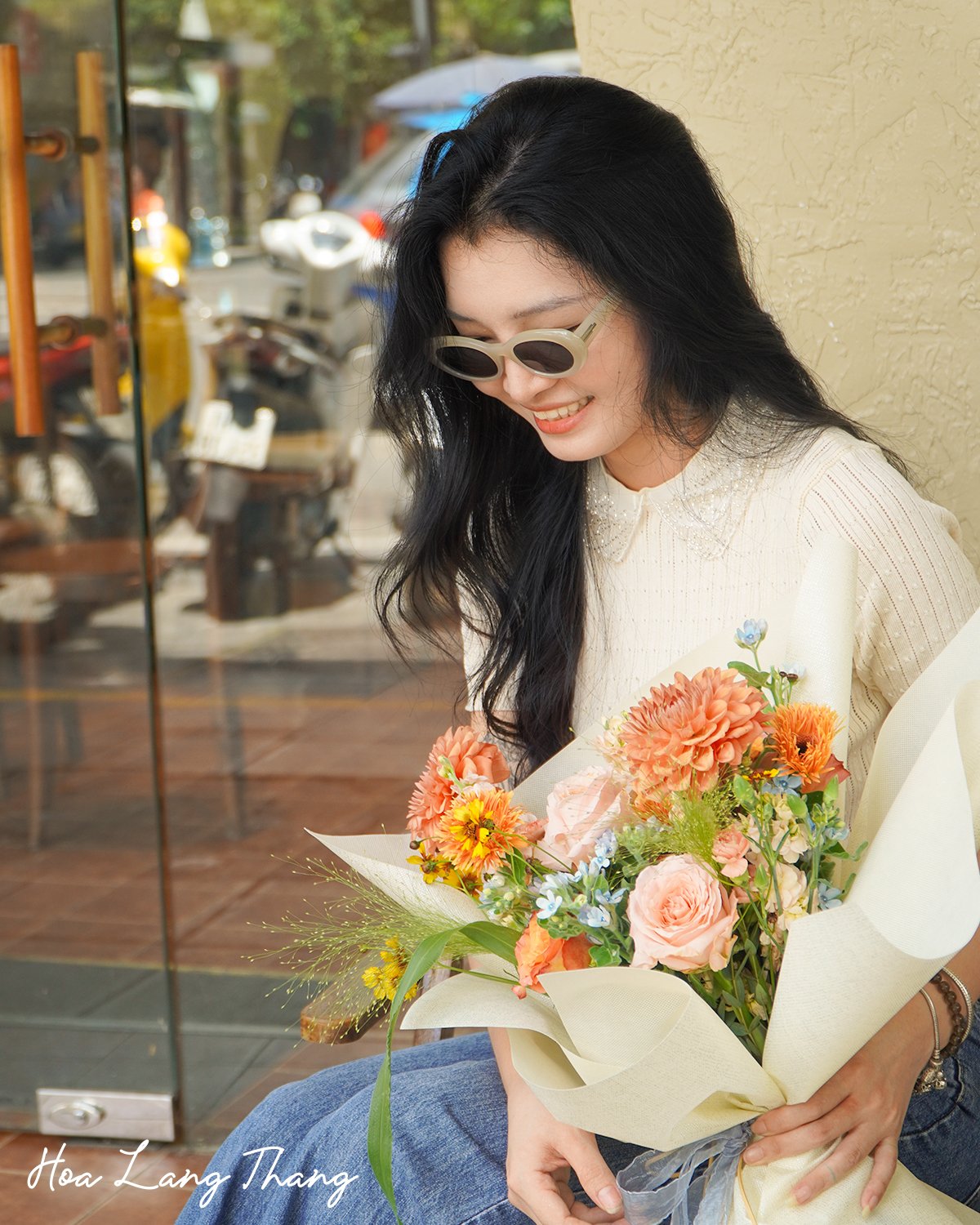 Cô gái trẻ cười tươi bên bó hoa đầy màu sắc, gồm hồng, cúc, và baby, kiểu cắm tự nhiên