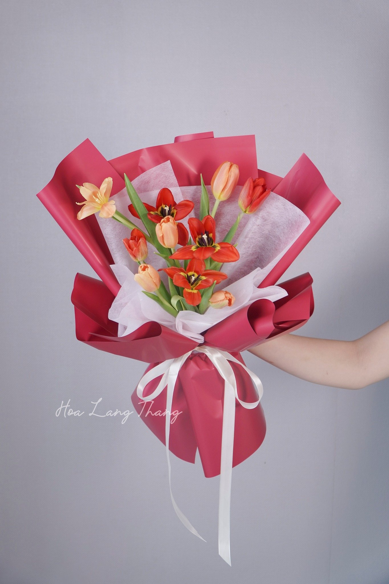 Bó hoa tulip và hoa hồng cam tươi mát trong giấy gói màu đỏ, trang trí nhẹ nhàng