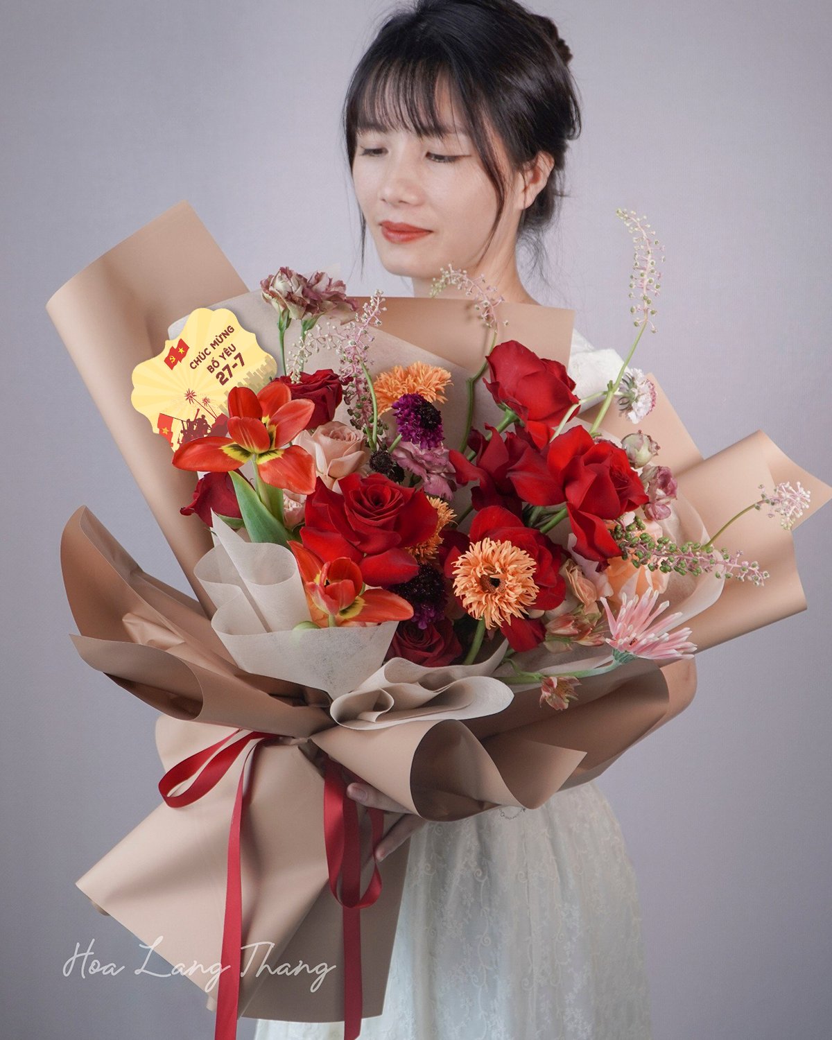 Một cô gái cầm bó hoa lớn với nhiều loại hoa như hồng, tulip, và ly, kiểu cắm nghệ thuật