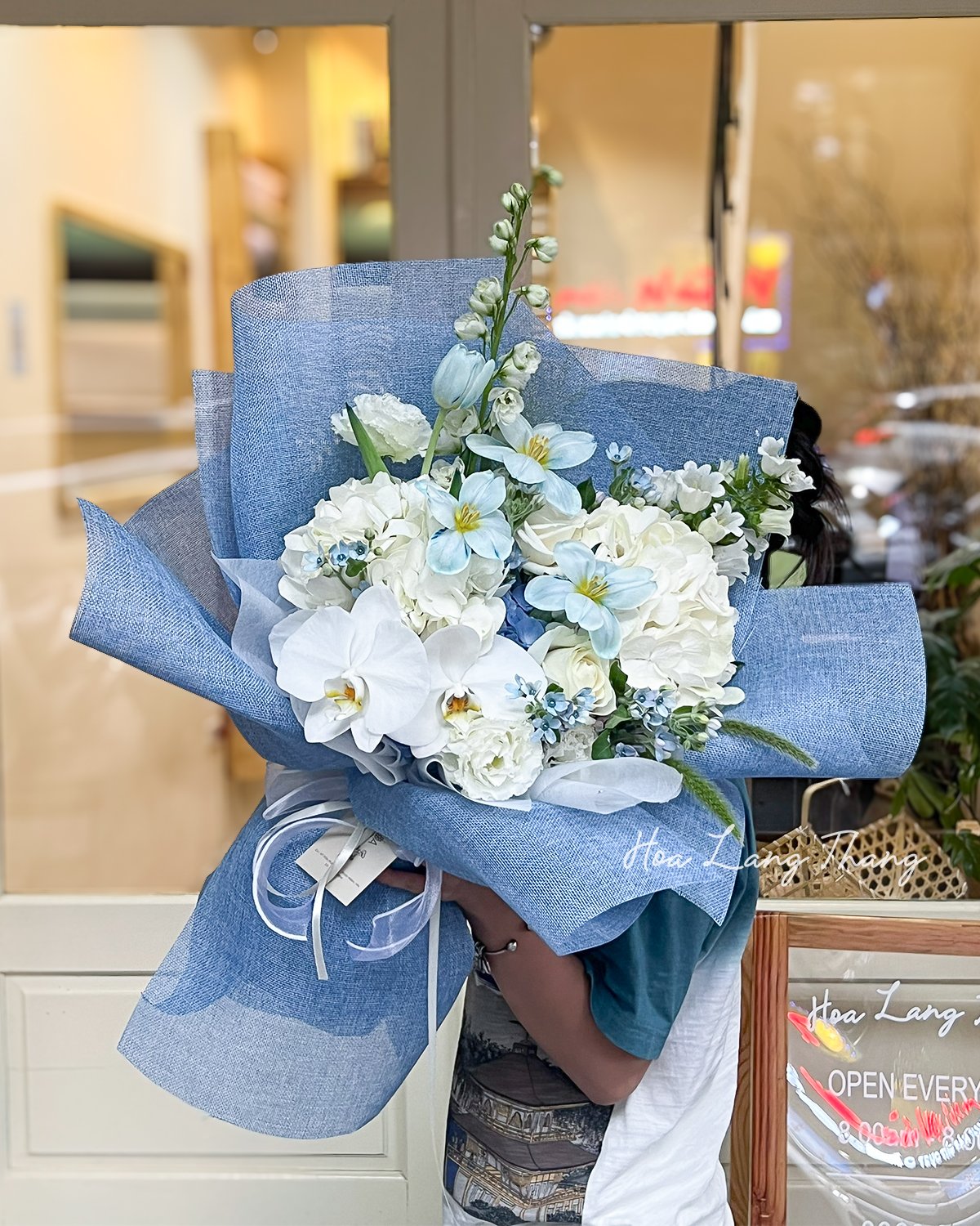 Bó hoa tươi nhiều loại, nổi bật với lan hồ điệp và tulip, màu xanh pastel nhẹ nhàng