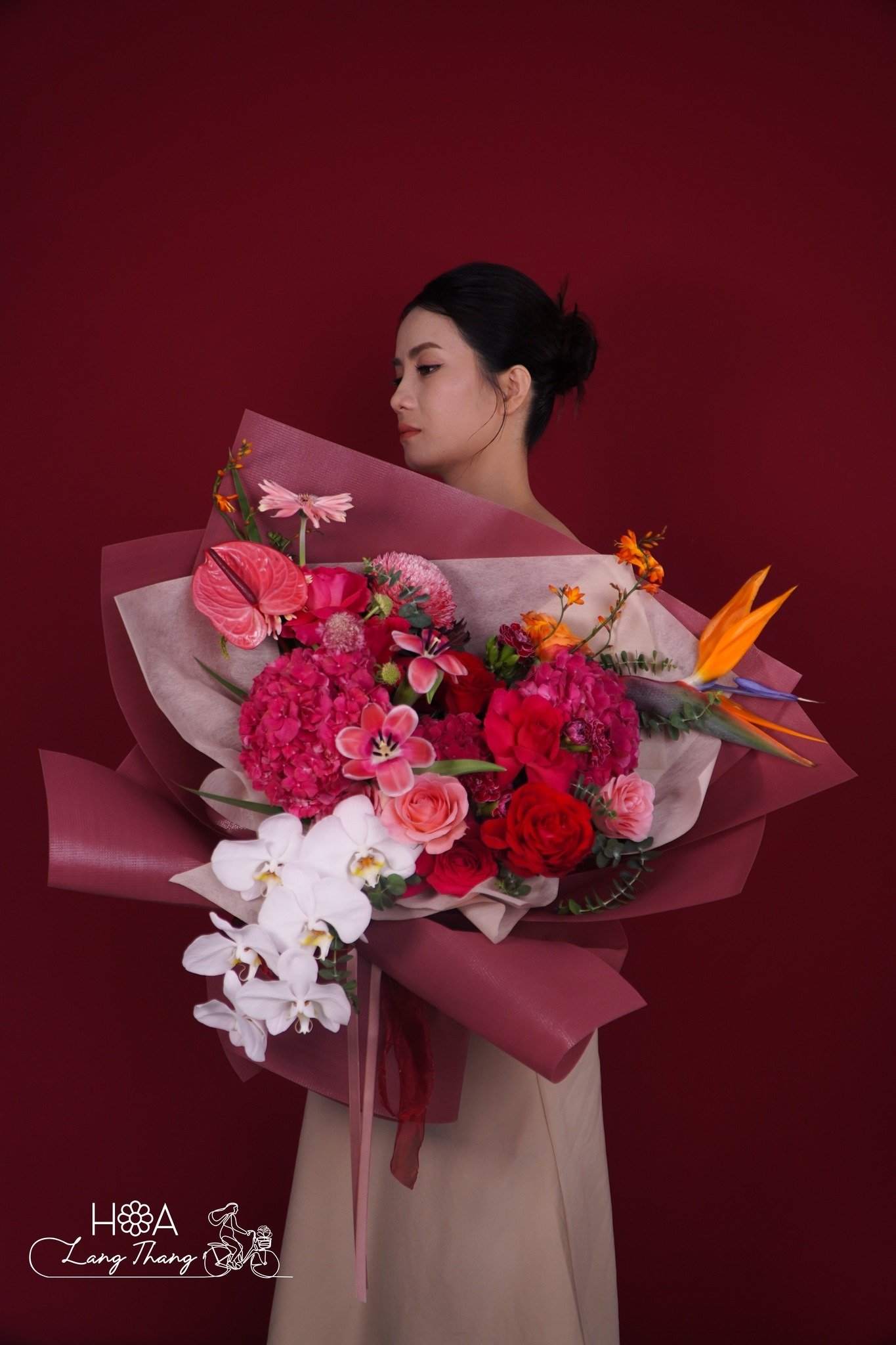Người phụ nữ cầm bó hoa lớn với hoa hồng, lan hồ điệp và hoa cẩm tú cầu, nổi bật trên nền đỏ