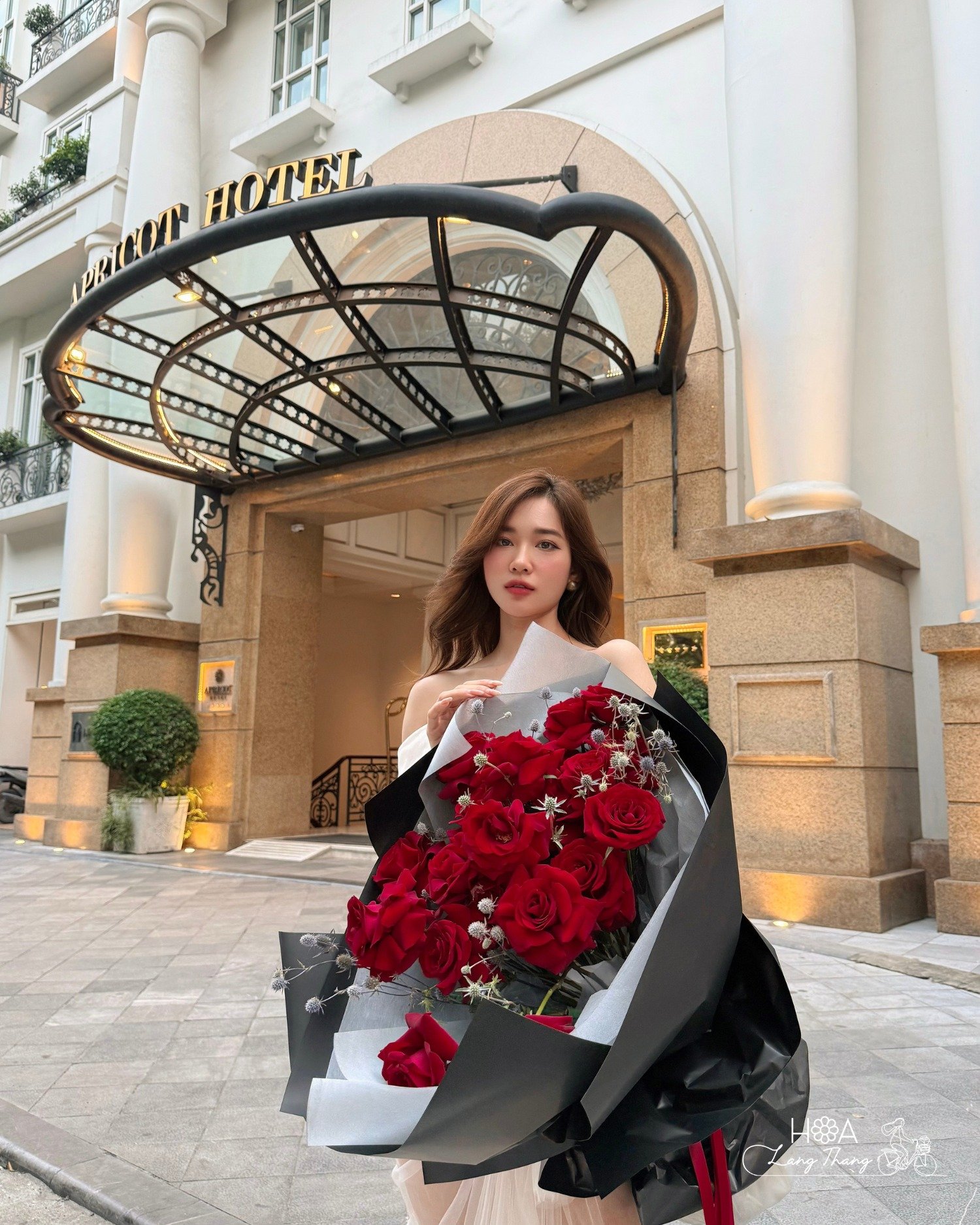 Cô gái cầm bó hoa hồng đỏ trước khách sạn sang trọng