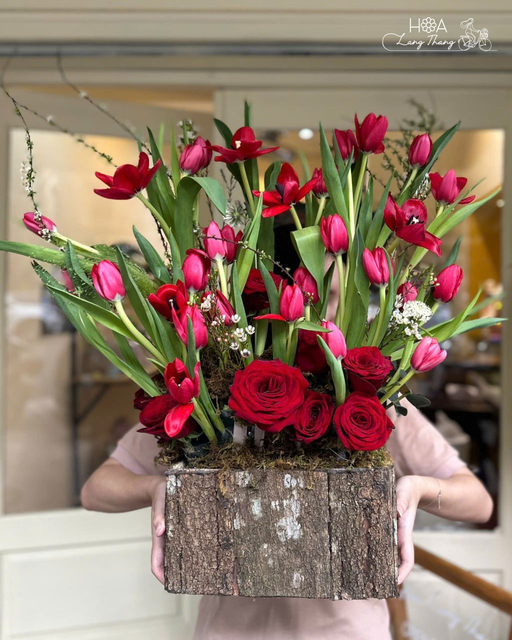 Bình hoa lớn với tulip đỏ, hoa hồng và cành xanh mát, kiểu cắm nghệ thuật