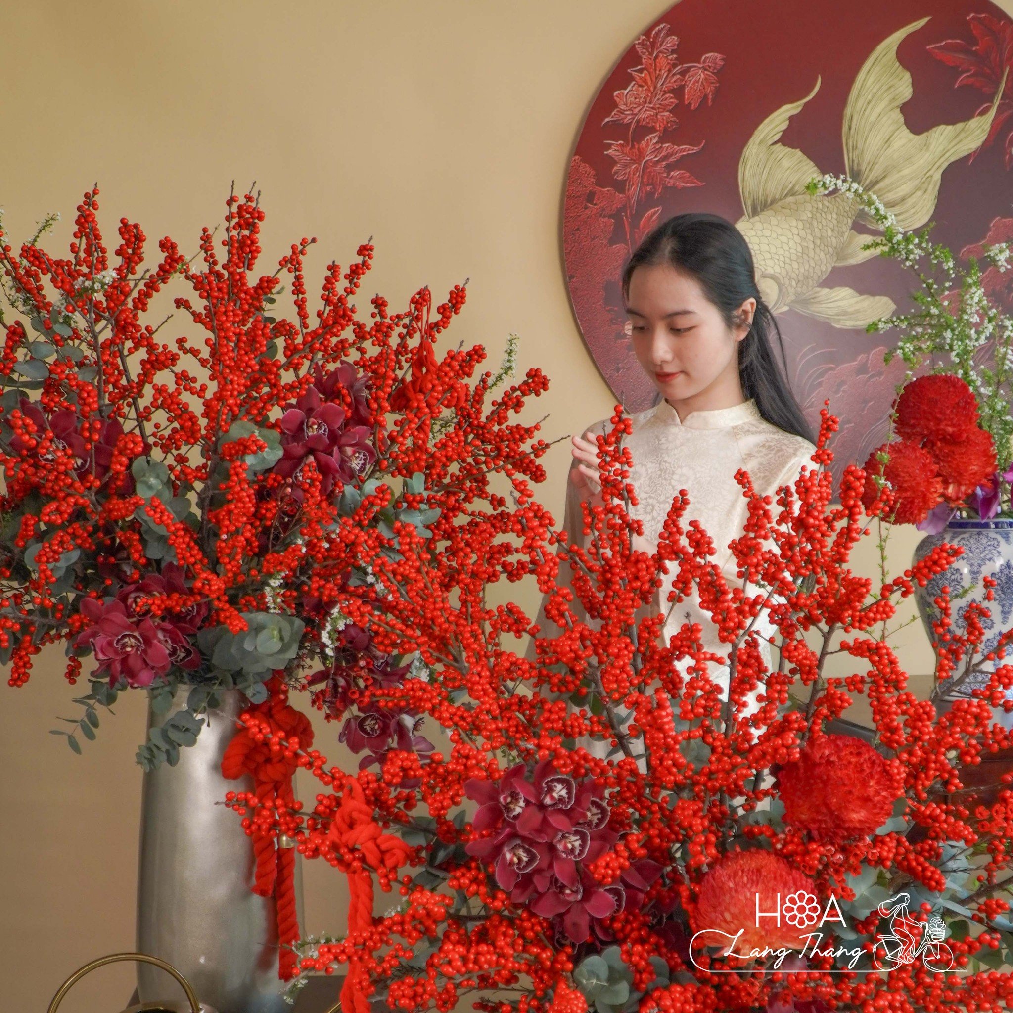 Cô gái trong chiếc áo dài giữa bình hoa lan hồ điệp đỏ rực rỡ, tạo không gian tươi mới