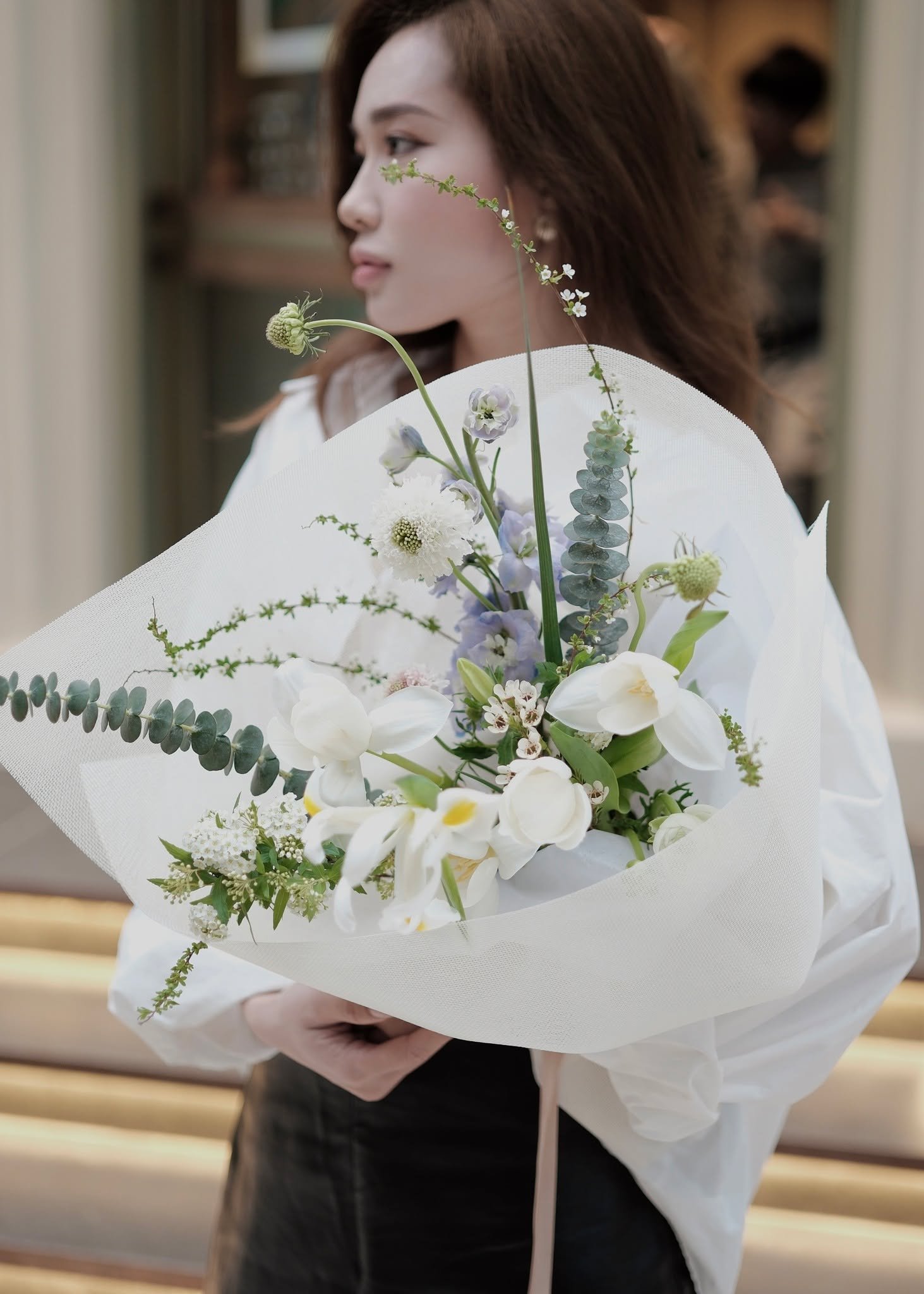 Người phụ nữ cầm bó hoa trắng, xanh, cắm sáng tạo với <a href=