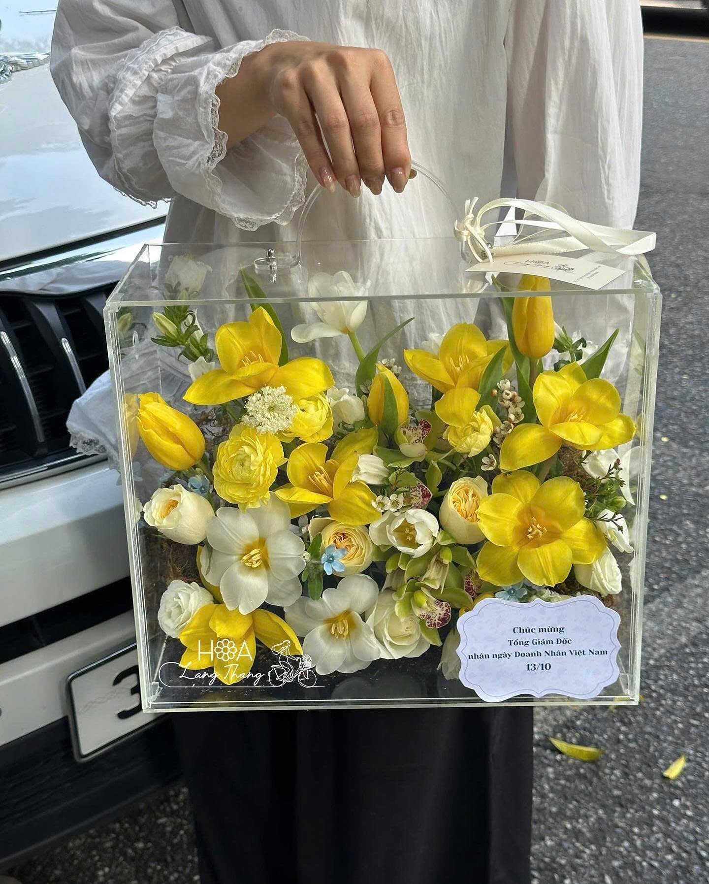 Bó hoa gồm tulip vàng, lan hồ điệp và hoa hồng trắng, được cắm trong hộp kính sang trọng