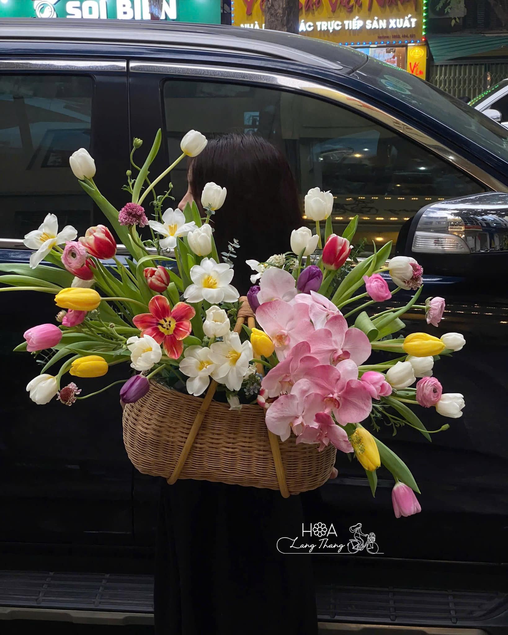 Bình hoa lớn với nhiều loại hoa như tulip và lan hồ điệp, được cắm tạo kiểu độc đáo