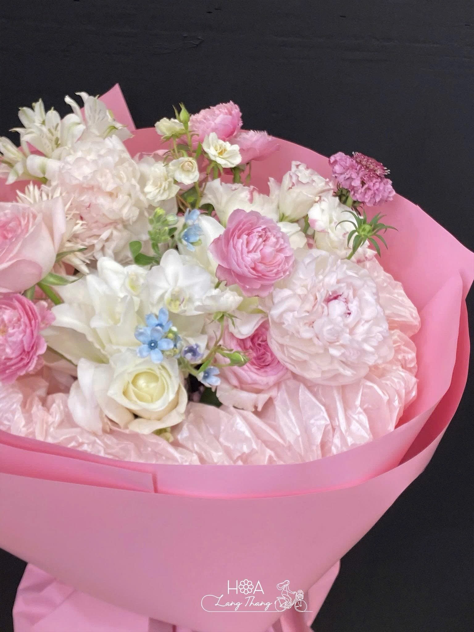 Bó hoa pastel gồm các loại hoa như hồng, tulip và hoa baby, cắm trong giấy hồng